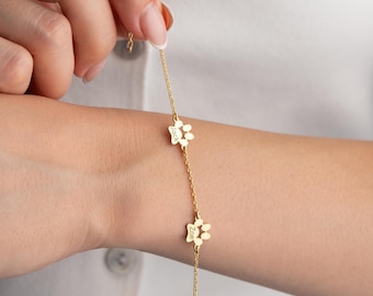 May include: Gold chain bracelet with two paw print charms. The charms are engraved with the names "Jack" and "Zoe".