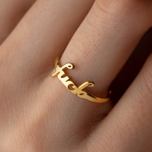 Puede incluir: Anillo de oro con la palabra "fuck" escrita en cursiva.