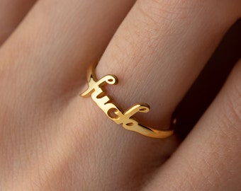 May include: Gold ring with the word "fuck" written in cursive.