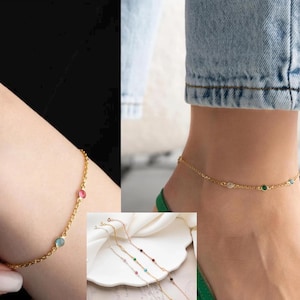 May include: Gold anklet with small colourful gemstones. The anklet is on a woman's ankle.
