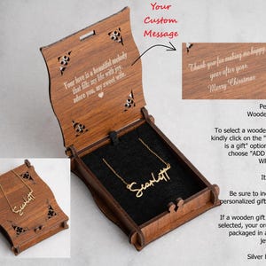 May include: A wooden gift box with a gold-colored necklace inside. The box is open, revealing a black interior and the necklace with the name "Scarlett". The box has decorative cutouts and text that reads "Your love is a beautiful melody..."