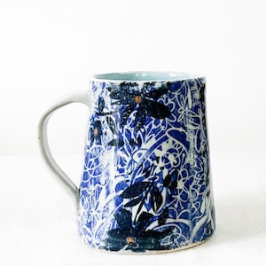 May include: A ceramic mug with a blue and white floral pattern. The mug features a light blue interior and a white handle. The design includes dark blue flowers and leaves against a white background, creating a striking contrast. This mug is perfect for coffee or tea.
