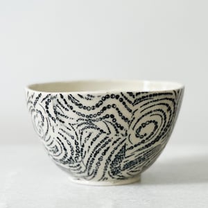 May include: A white ceramic bowl with a black and white swirl pattern. The pattern is made up of small dots and lines.