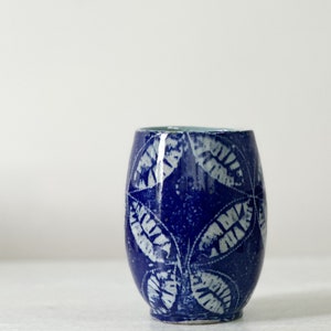 May include: A blue ceramic cup with a white leaf pattern. The cup is glazed and has a rounded shape.