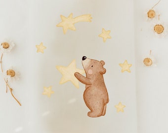 May include: A watercolor illustration of a brown bear holding a yellow star. The bear is surrounded by yellow stars, including a shooting star. The illustration is on a white background.