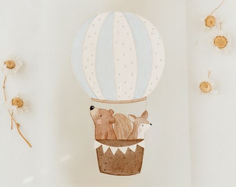 May include: A watercolor illustration of a blue and white hot air balloon with a brown bear and a fox inside. The balloon is surrounded by dried flowers on a white background.