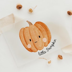 Könnte beinhalten: Eine Aquarell-Illustration eines niedlichen orangefarbenen Kürbisses mit einem lächelnden Gesicht. Der Kürbis befindet sich auf einem weißen Hintergrund mit dem Text "little pumpkin" darunter.