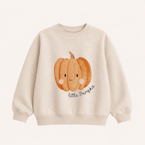 Könnte beinhalten: Ein beiges Langarm-Sweatshirt mit einer Aquarell-Illustration eines orangefarbenen Kürbisses mit lächelndem Gesicht und rosa Wangen. Der Text "little Pumpkin" ist in schwarzer Schreibschrift unter der Grafik aufgedruckt.
