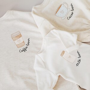 Könnte beinhalten: Drei weiße T-Shirts mit verschiedenen Designs. Das erste Shirt hat eine Kaffeetasse mit dem Text "Coffee Lover". Das zweite Shirt hat eine Milchflasche mit dem Text "Milk Lover". Das dritte Shirt hat eine Kakaotasse mit dem Text "Cocoa Lover".