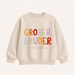 Könnte beinhalten: Ein beigefarbener Pullover mit Rundhalsausschnitt und dem Text GROBER BRUDER in großen, bunten, abgerundeten Buchstaben. Unter dem Haupttext steht der Schriftzug Better together in einer kleineren, schlichten Schrift mit einem Herz.