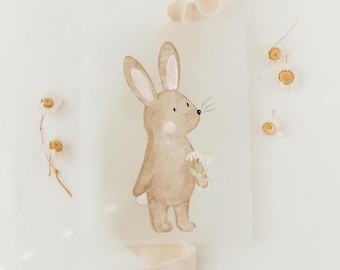 May include: A watercolor illustration of a brown bunny holding a bouquet of white flowers. The bunny is standing on a white background with dried flowers scattered around it.