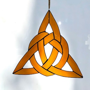May include: A gold-colored stained glass Celtic knot, also known as a Trinity knot, in the shape of a triangle. The knot is made of three interlocked loops, symbolizing the interconnectedness of life.