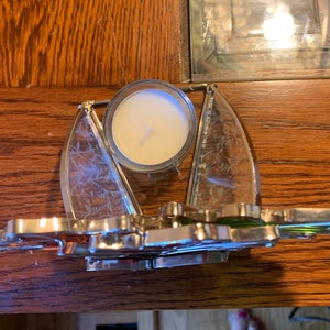 May include: A silver candle holder with a clear glass insert for a tea light candle. The holder is shaped like a sailboat with a green and orange sail.