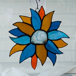 May include: A stained glass suncatcher with a blue and gold flower design. The center of the flower is a round, white agate stone.