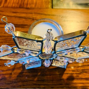 May include: A clear glass snowflake candle holder with crystal accents. The holder is designed to hold a tea light candle.