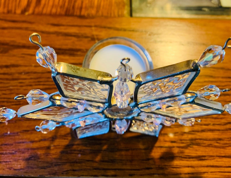 May include: A clear glass snowflake candle holder with crystal accents. The holder is designed to hold a tea light candle.