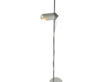 Pode incluir: Uma luminária de chão moderna com uma cabeça de lâmpada cilíndrica branca e um braço ajustável cromado. A lâmpada tem um poste fino cinza escuro e uma base circular. O cabo elétrico é branco. Para uso interno.