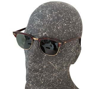 May include: Sunglasses with a classic design. The frames are a dark brown color with gold-colored accents and green lenses. The sunglasses are displayed on a mannequin head.