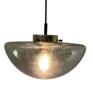 Op de afbeelding: Een hanglamp van messing en glas met een heldere, gematteerde glazen kap. De lamp hangt aan een zwart snoer.
