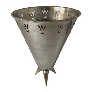 Pu&ograve; includere: Un vaso di forma conica in argento con un motivo decorativo a taglio e tre gambe appuntite.