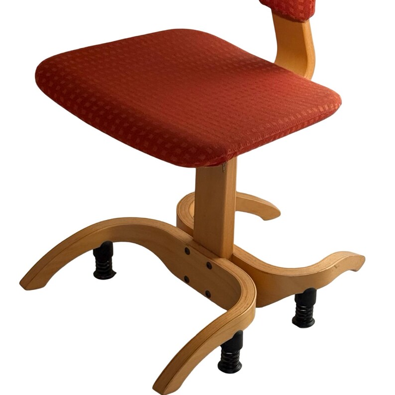 Puede incluir: Una silla de madera vintage con asiento y respaldo estampados en rojo. La silla tiene un marco de madera clara con patas curvas y una columna de soporte central. Las patas tienen pies ajustables negros.