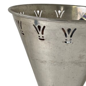 Pu&ograve; includere: Secchiello per il ghiaccio in metallo argentato con un design decorativo tagliato. Il secchiello ha una parte superiore larga e svasata e una base stretta.