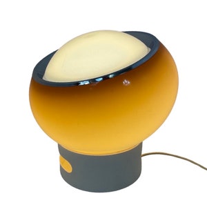 May include: A vintage table lamp with a yellow and white glass shade and a gray base. The shade has a chrome trim around the top edge.