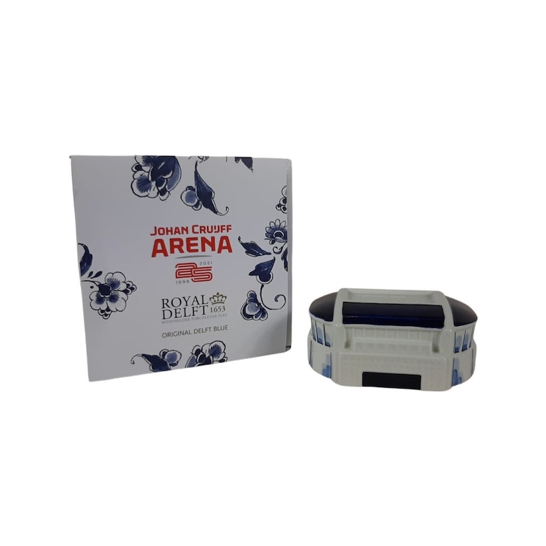 May include: A white and blue ceramic model of the Johan Cruyff Arena, a football stadium in Amsterdam, Netherlands. The model is decorated with traditional Dutch Delft blue patterns. The box features the stadium's name and the Royal Delft logo.