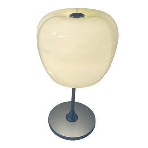 Op de afbeelding: Een witte tafellamp in de vorm van een appel met een zilveren voet en steel.