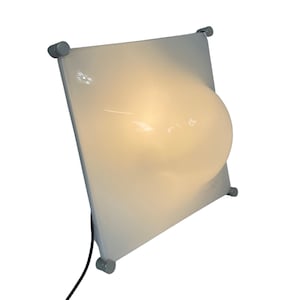 Könnte beinhalten: Eine weiße Wandleuchte mit abgerundeter, bauchiger Form. Die Lampe hat ein silbernes Kabel und vier silberne Befestigungspunkte.