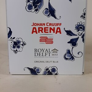 May include: A white box with a blue and white floral design. The box features the text "Johan Cruijff Arena 1996 2021" and a red logo with the number 25. The box also features the text "Royal Delft 1653 Koninklijke Porceleine Fles Original Delft Blue".