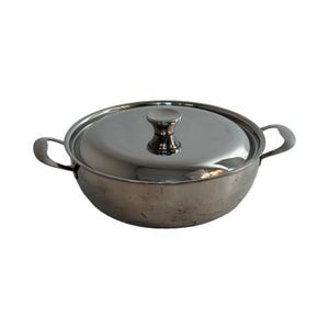 Op de afbeelding: Een roestvrijstalen pan met een deksel en een knop bovenop. De pan heeft twee handvatten aan de zijkanten.