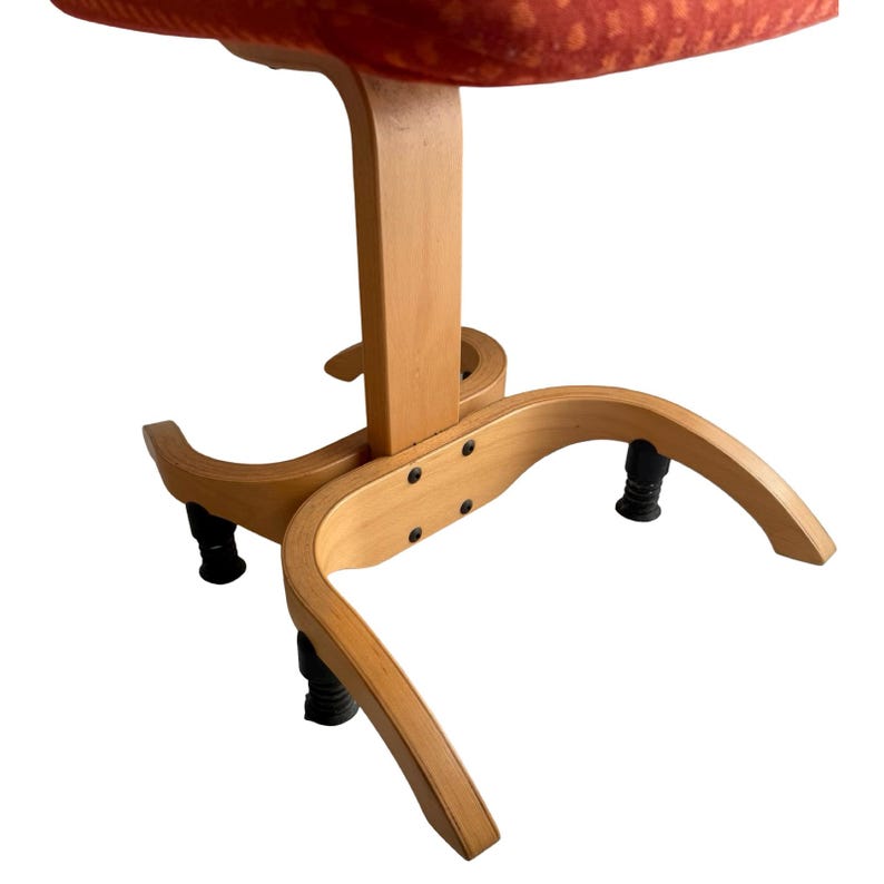 Puede incluir: Una silla vintage con estructura de madera clara y asiento naranja estampado. La silla tiene una base curva con patas negras y una columna de soporte central. El asiento tiene un patr&oacute;n texturizado.
