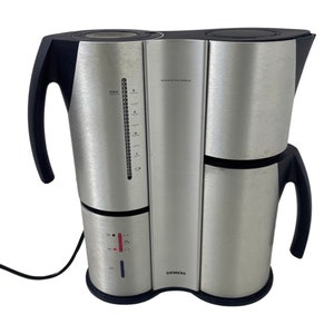 May include: A silver and black coffee maker with a sleek, modern design. The appliance features a water level indicator, a power switch, and the text "DESIGN BY F.A. PORSCHE" and "SIEMENS". The coffee maker has a capacity for up to 8 cups.