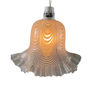 May include: A white glass pendant light with a ruffled edge and a striped pattern. The light is turned on and emits a warm glow.