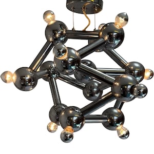 Puede incluir: Una lámpara de araña cromada con un diseño único de estructura atómica. La lámpara presenta múltiples bombillas esféricas conectadas por varillas rectas, creando un patrón geométrico. Las bombillas están encendidas, emitiendo un brillo cálido.