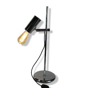 May include: A chrome desk lamp with a single bulb and a round base. The lamp has a long, adjustable arm that can be positioned to direct the light.