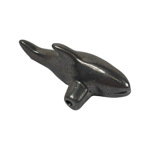 May include: A small, silver-coloured, orca whale figurine. The figurine is detailed with a fin, tail, and a small eye.