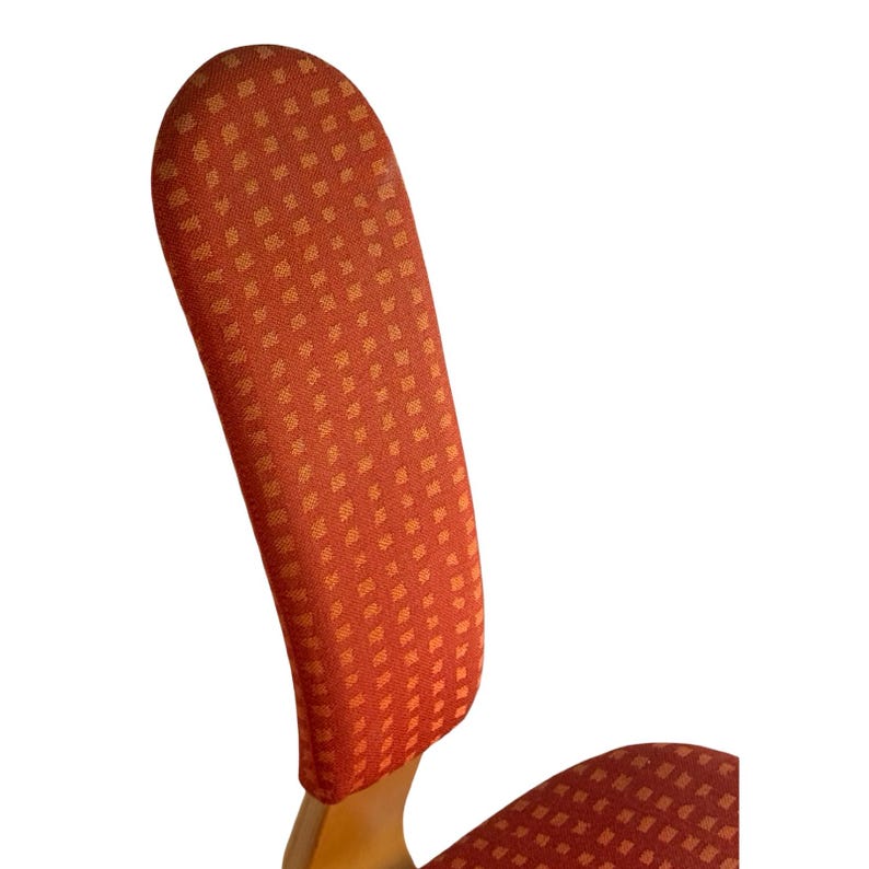 Puede incluir: Primer plano del respaldo de una silla con un dise&ntilde;o curvo. El respaldo de la silla est&aacute; tapizado en una tela roja con un patr&oacute;n cuadrado repetido en un tono m&aacute;s claro de rojo. El marco de madera es visible en la base.