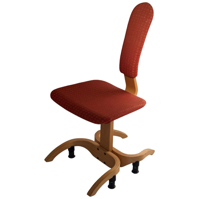 Puede incluir: Una silla de escritorio de madera con respaldo y asiento curvos tapizados en tela naranja rojiza estampada. La silla tiene una estructura de madera clara y patas negras. El dise&ntilde;o recuerda a los muebles modernos de mediados de siglo.