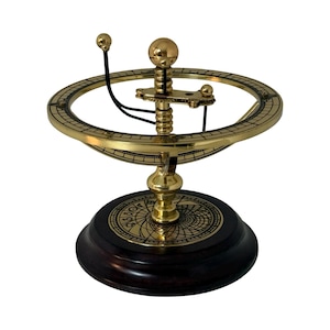 May include: A brass armillary sphere model featuring a central vertical axis with a large sphere at the top, surrounded by a horizontal ring with engraved markings. The base is a dark circular wood stand with a brass inlay showing celestial symbols.