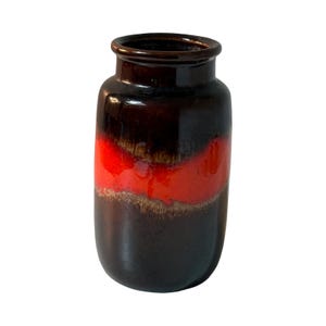 Puede incluir: Un jarrón de cerámica vintage con acabado brillante. El jarrón presenta una parte superior e inferior marrón oscuro con una banda roja vibrante en el medio. El diseño es un contraste llamativo de colores y texturas, adecuado para la decoración del hogar.