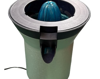 May include: A silver-colored electric citrus juicer with a black handle and a blue reamer. The juicer has a circular design with a black rim and the brand name "SIEMENS" printed on the front.