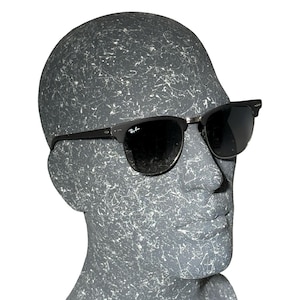 May include: Black sunglasses with dark lenses and a silver bridge. The sunglasses have a classic design with a black frame and are displayed on a grey mannequin head.