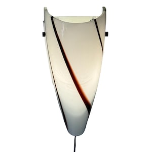 May include: A white wall sconce with a curved top and a tapered bottom. The sconce has a translucent appearance with brown and black diagonal stripes. A black power cord extends from the bottom.