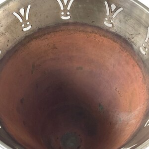 Pu&ograve; includere: Una ciotola d'argento con interno in rame. La ciotola ha un design decorativo attorno al bordo con corone stilizzate bianche.