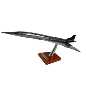 May include: A silver model of a Concorde supersonic jet airplane on a wooden base. The model is in flight position with the nose pointed upwards.