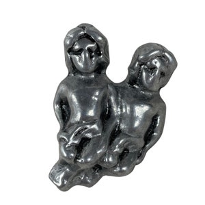 Op de afbeelding: Een tinnen beeldje van het sterrenbeeld Tweelingen, met twee figuren die rug aan rug staan.