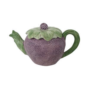 Op de afbeelding: Een paarse en groene theepot van keramiek in de vorm van een bes met een bladerdeksel.