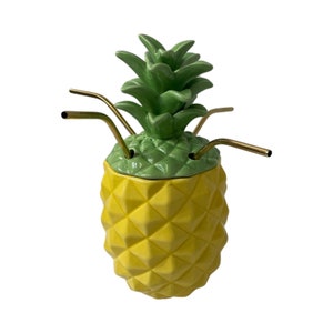 Könnte beinhalten: Eine gelbe Keramik-Ananas-Tasse mit grünem Ananas-Deckel und vier goldenen Metall-Strohhalmen.